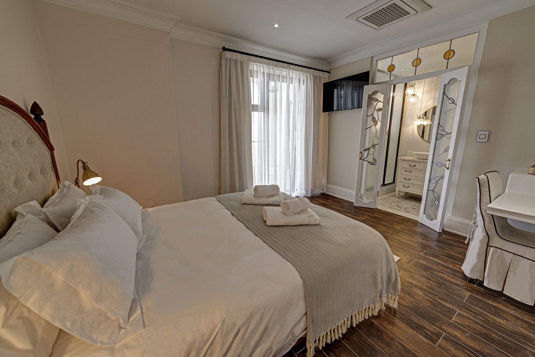 A hotel room with a large bed, a desk, a bathroom with a mirror, and a shower area.