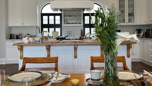 A modern kitchen with white cabinetry, a central island, and a dining area set for four. - Lagoon Suites Boutique Hotel (Walvis Bay)