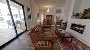 A spacious living room with a leather sofa, a coffee table, and a fireplace. There is a dining area with chairs and a table in the background. - Lagoon Suites Boutique Hotel (Walvis Bay)