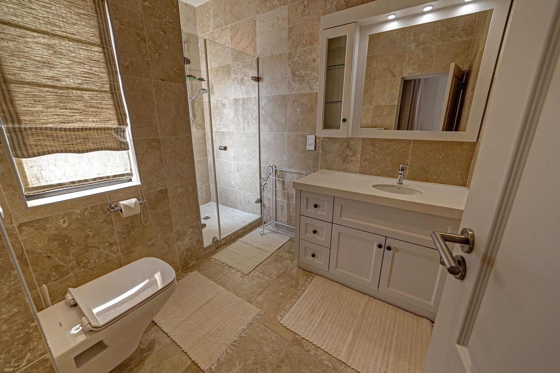 Un baño moderno con cabina de ducha de vidrio, inodoro, lavamanos con espejo y toallero.