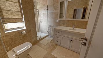 Un baño moderno con cabina de ducha de vidrio, inodoro, lavamanos con espejo y toallero.