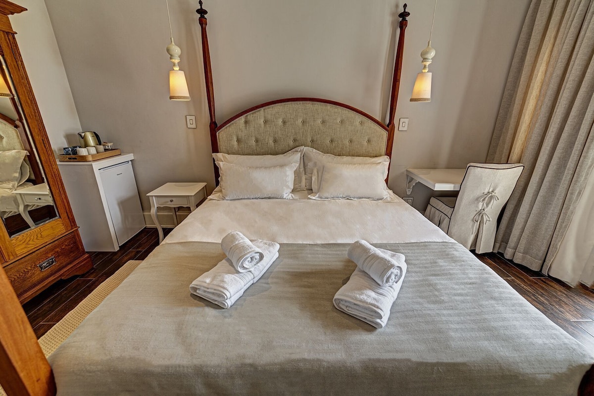 A neatly made bed with two rolled towels, a wooden headboard, bedside tables, and a mirror.