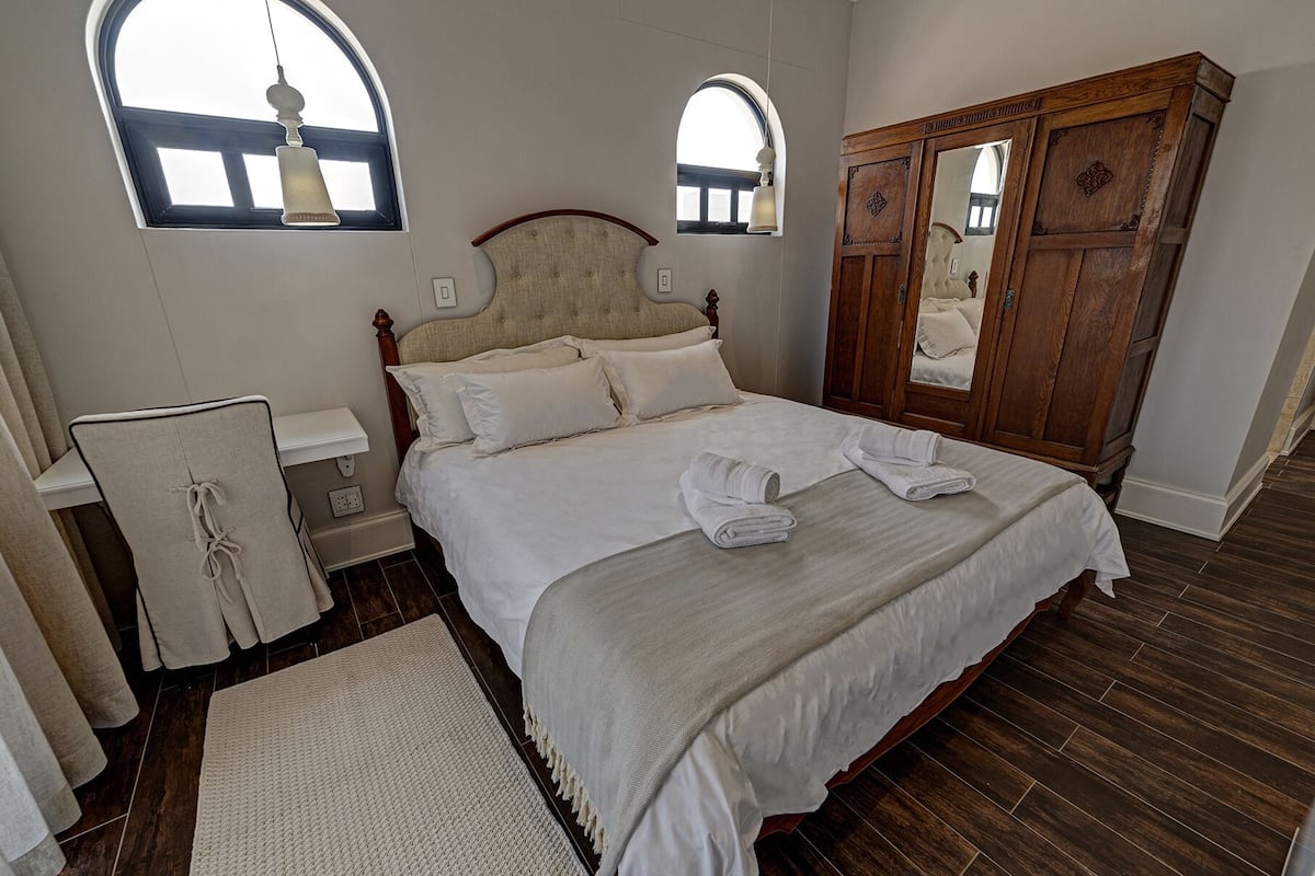 A bedroom with a large bed, a wooden wardrobe, two bedside tables, and a chair.