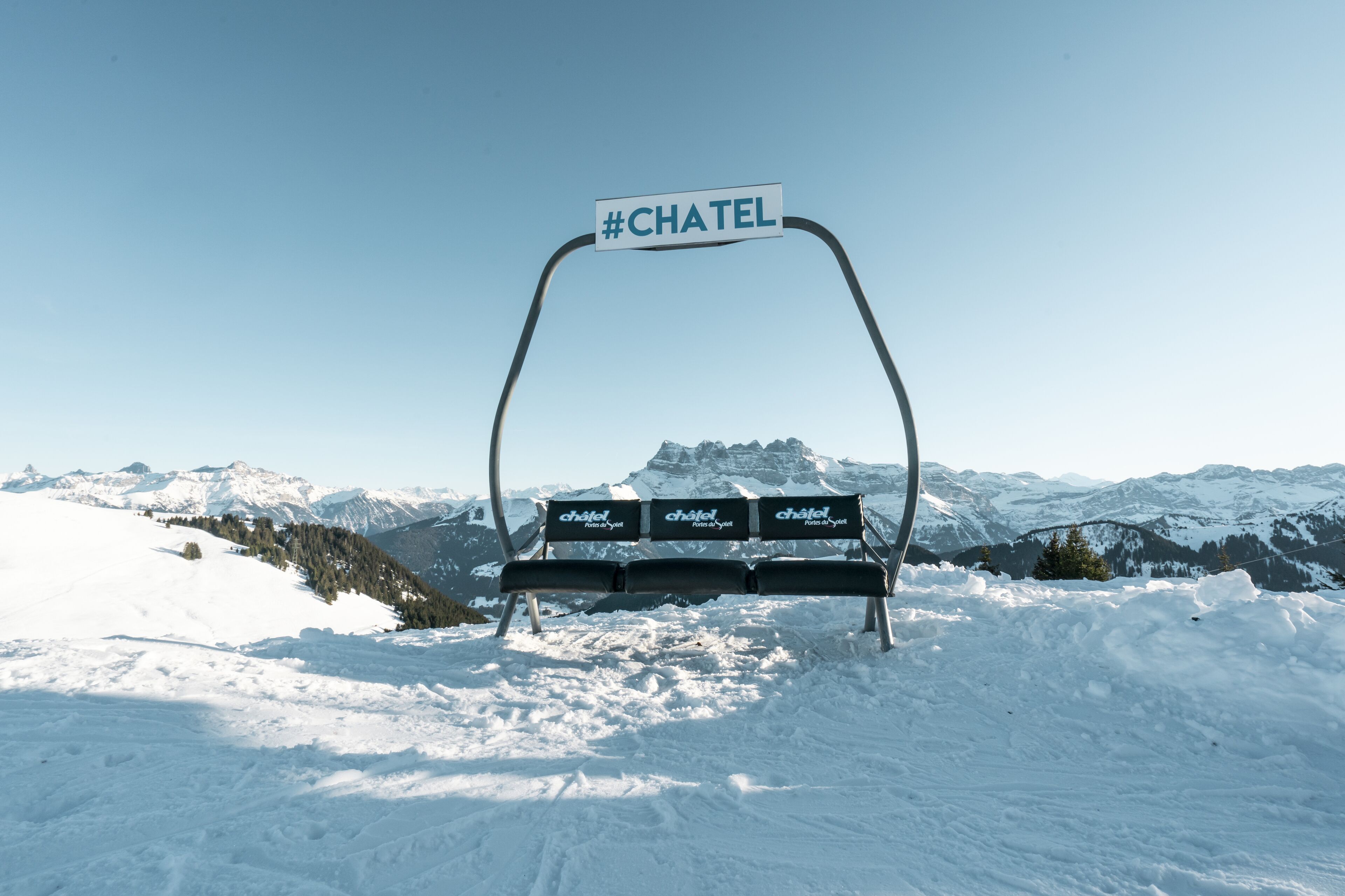 Une montagne enneigée, avec un banc et un panneau indiquant « #CHATEL » au premier plan.