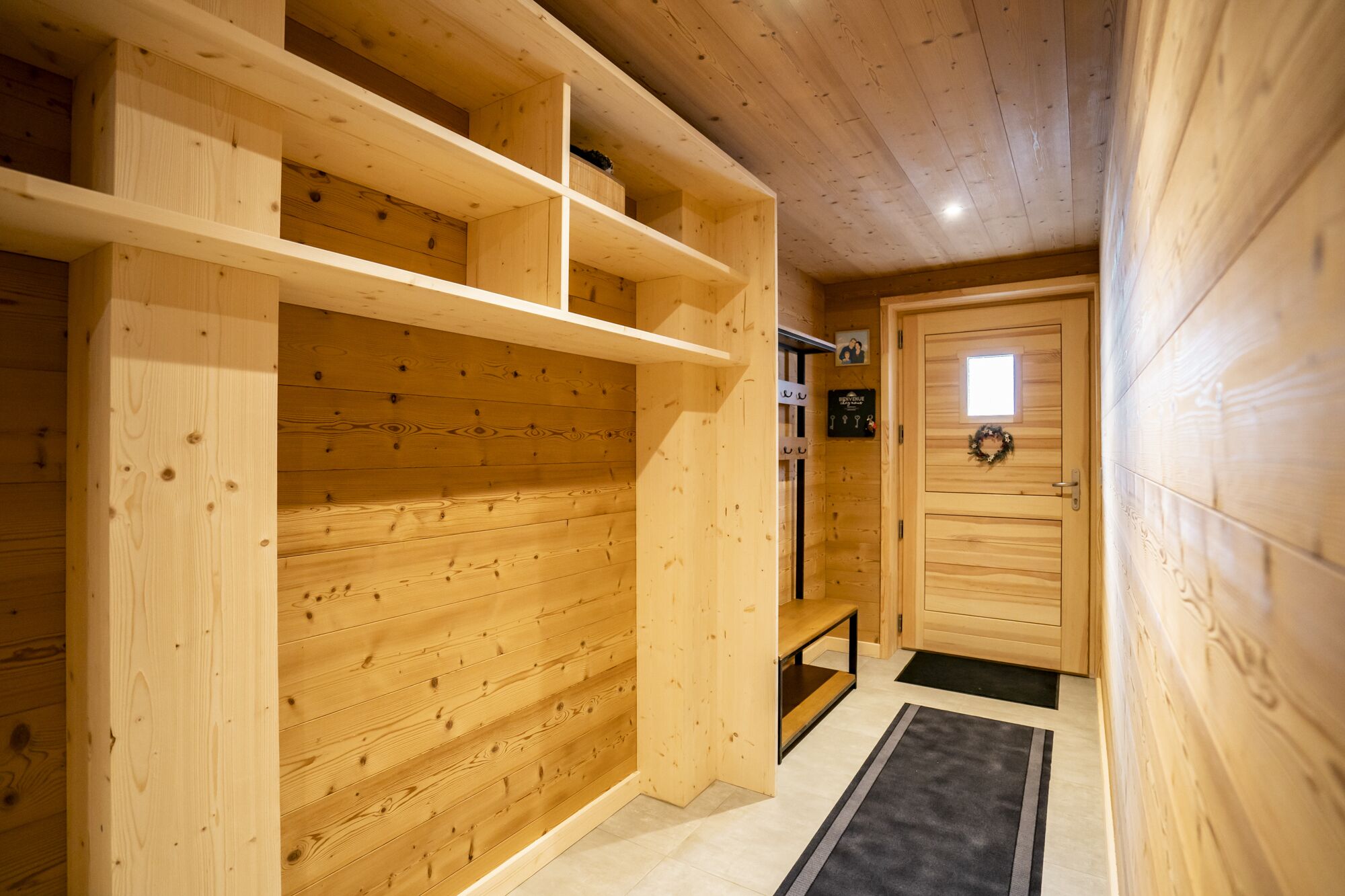 A wooden interior with built-in shelves, a door with a small window, and a black mat at the entrance.
