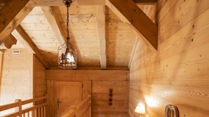 A wooden interior with a staircase, wooden railings, and a hanging light fixture.