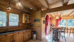 A wooden cabin interior with a kitchen and dining area, featuring wooden cabinets, a sink, and a dining table with chairs.