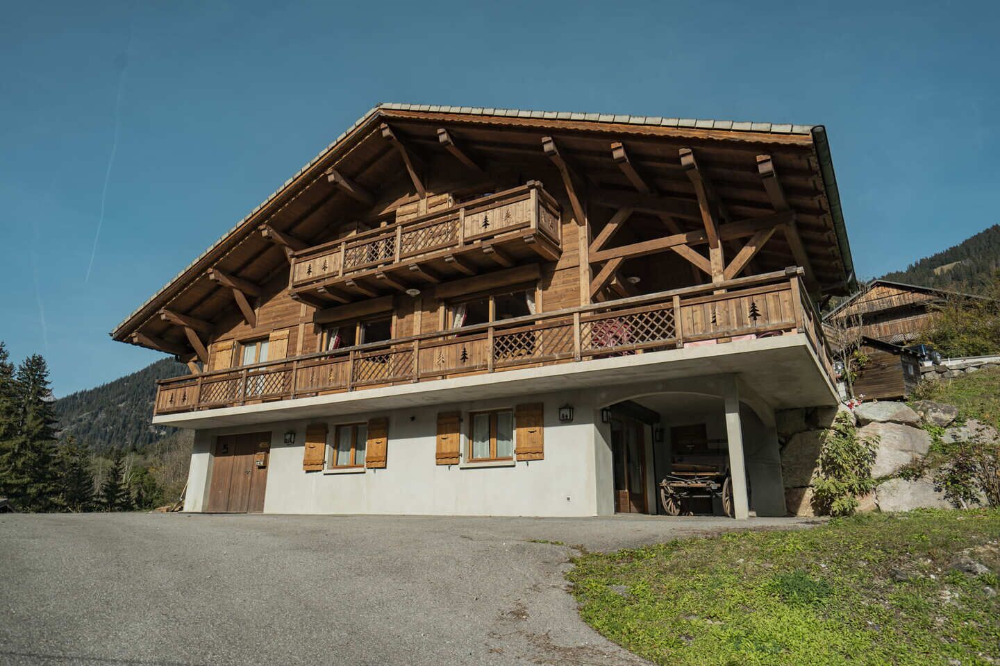 A two-story wooden chalet with a balcony, a front entrance, and a stone foundation.
