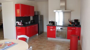 A compact kitchen with red cabinets, a stainless steel refrigerator, and a modern stove. - Les Demeures de la BeauClaire - Provençal Elegance, Pool, Air Conditioning, Warm Hospitality (Piolenc)