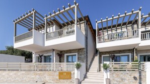 Un edificio moderno de dos pisos con balcones, fachada de piedra y un letrero que indica que es un hotel.