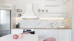 Una cocina moderna con armarios blancos, salpicadero de mármol y una isla central con fregadero y cafetera.