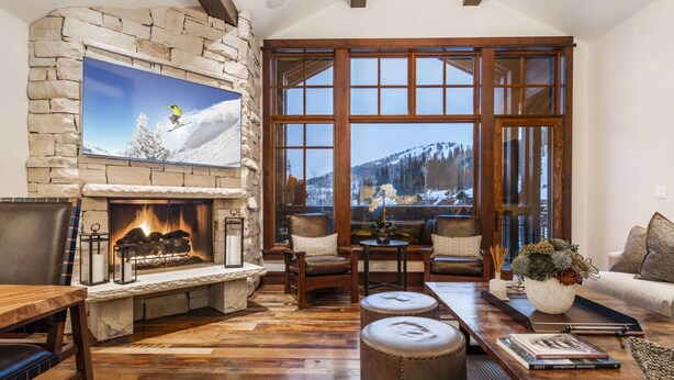 Una sala de estar acogedora con chimenea de piedra, mobiliario de cuero y un ventanal con vistas a la montaña.