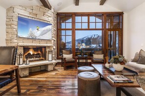 A cozy living room with a stone fireplace, leather furniture, and a large window offering a mountain view. - Empire Pass Penthouse
Ski-in/Ski-Out at Deer Valley (Park City)