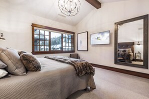 Une chambre à coucher avec un grand lit, une fenêtre donnant sur un paysage enneigé, un lustre et un miroir qui reflète le lit.