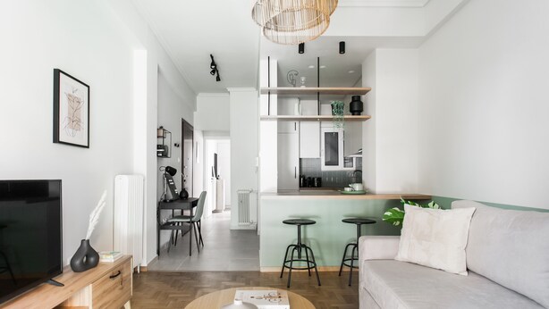 Sala moderna com sofá, mesa de centro e televisão. Há uma área de cozinha com banquetas e mesa de jantar.