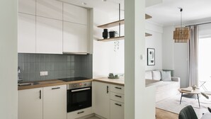 Cozinha moderna com armários brancos, forno embutido e bancada de madeira. Há uma sala de jantar com mesa e cadeiras, e uma sala de estar com sofá e mesa de centro.