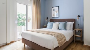 Quarto com cama grande, piso de madeira, porta de vidro deslizante para uma varanda e quadro pendurado na parede.