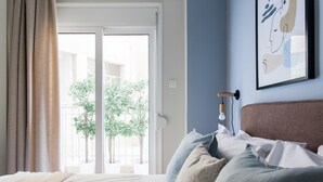 Quarto com cama, janela com cortinas, luminária na parede e uma obra de arte emoldurada.