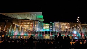 A large building with a modern architectural design, featuring a prominent glass facade and a series of water fountains in the foreground. - Cozy apartment n Stavros Niarchos Park (Kallithea)