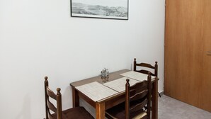 A dining area with a wooden table and chairs, a framed picture on the wall, and a wooden door. - Cozy apartment n Stavros Niarchos Park (Kallithea)