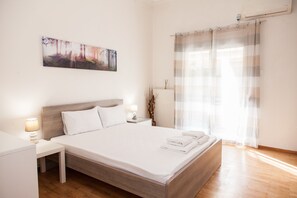 A modern hotel room with a large bed, a nightstand, a lamp, a painting on the wall, and a window with curtains. - Cozy apartment n Stavros Niarchos Park (Kallithea)