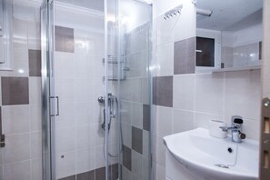 A modern bathroom with a glass shower enclosure, a white sink with a mirror, and a tiled wall with a mix of white and gray tiles. - Cozy apartment n Stavros Niarchos Park (Kallithea)