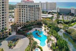 Un resort con varios edificios altos, una piscina central y una zona ajardinada con palmeras.