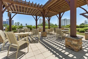 Un patio al aire libre con mesas y sillas, pilares de piedra y una pérgola de madera.