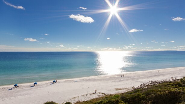 Ein Strand mit blauem Himmel, strahlender Sonne und ruhigem Wasser.