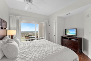Habitación de hotel con una cama grande, televisión, balcón con vistas y ventilador de techo.