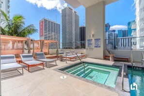 Relax by the rooftop pool with a stunning city view, surrounded by lounge chairs and a wooden pergola.