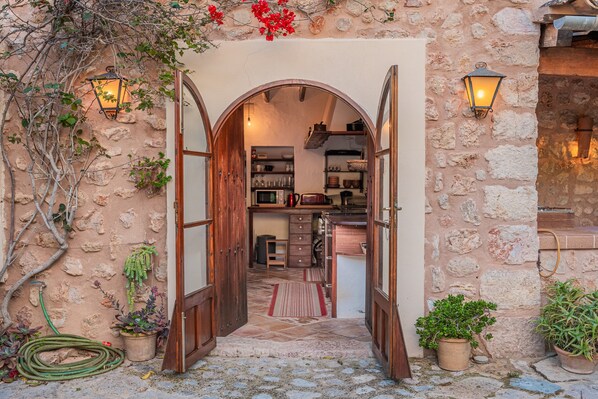 An arched doorway leading to a kitchen with stone walls, wooden cabinets, and hanging plants.