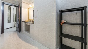 A bathroom with a marble wall, a sink, and a mirror. There is a black metal shelf with a towel on it.