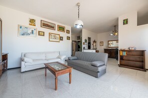 Uma sala de estar com um sofá branco, um sofá cinza, uma mesa de centro de madeira e uma estante de livros.