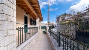 Un edificio de piedra con balcón, un camino empedrado y un muro de piedra con una valla.