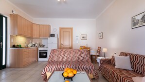 A modern kitchen with wooden cabinets, a dining area with a patterned sofa, and a coffee table with oranges. - Apartment "Villa Votistis A1" with Mountain View, Garden & Wi-Fi (Lefkadas)