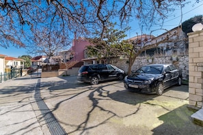 Una calle residencial con autos estacionados, un muro de piedra y un árbol sin hojas.