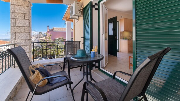 A balcony with a table and chairs, a view of the city, and a green shuttered door. - Apartment "Villa Votistis A1" with Mountain View, Garden & Wi-Fi (Lefkadas)