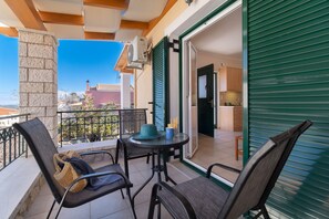 Een balkon met een tafel en stoelen, een uitzicht op de stad, en een deur met groene luiken.