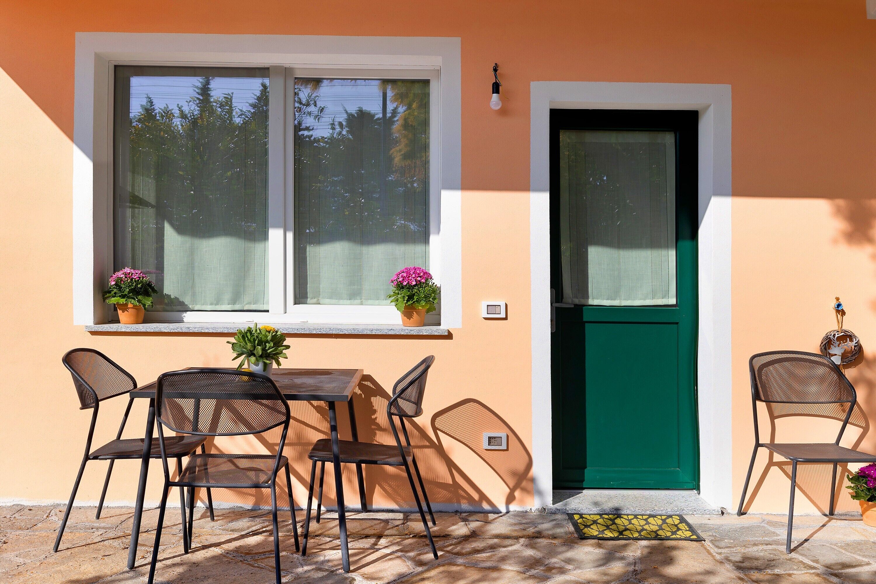 A room with a table and chairs, a window with plants, and a green door.