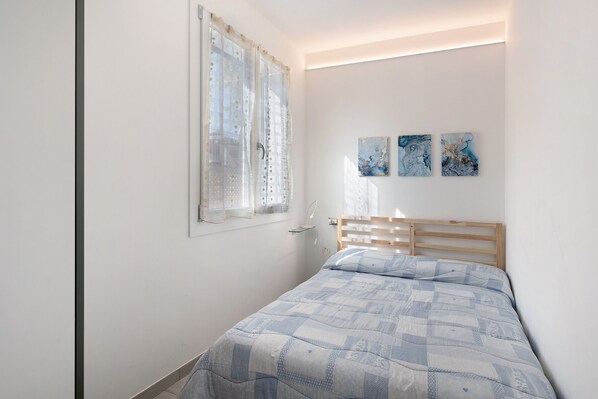 Ein Schlafzimmer mit Bett, Fenster mit Vorhängen und zwei an der Wand befestigten Kunstwerken.