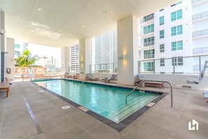Una piscina interior con suelo de baldosas, sillones de descanso y vistas a un edificio alto.