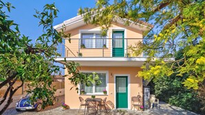 Um edifício de dois andares com varanda, uma porta verde e um pequeno espaço de pátio com mesa e cadeiras.