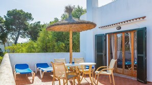 Une terrasse avec des chaises et une table, un parasol en chaume et une porte avec des volets.