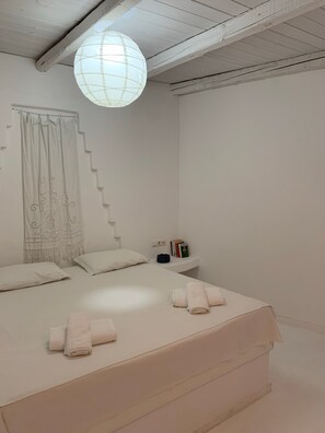 Een minimalistische slaapkamer met een bed, een nachtkastje met boeken en een hanglamp.