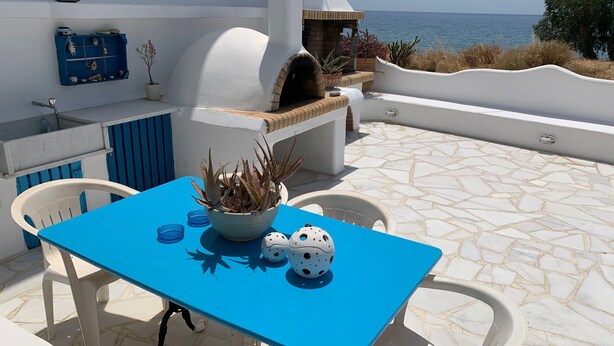 Een blauwe tafel met een potplant, twee witte Crocs-sandalen en een witte bank.