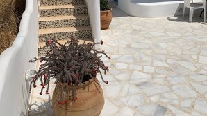 Een wit gebouw met een trap naar een blauwe deur, een plant in een pot en een tafel met een stoel.
