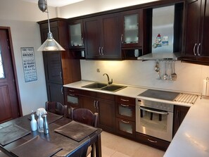 Een moderne keuken met donkerhouten kasten, roestvrijstalen apparatuur en een eethoek met een tafel en stoelen.