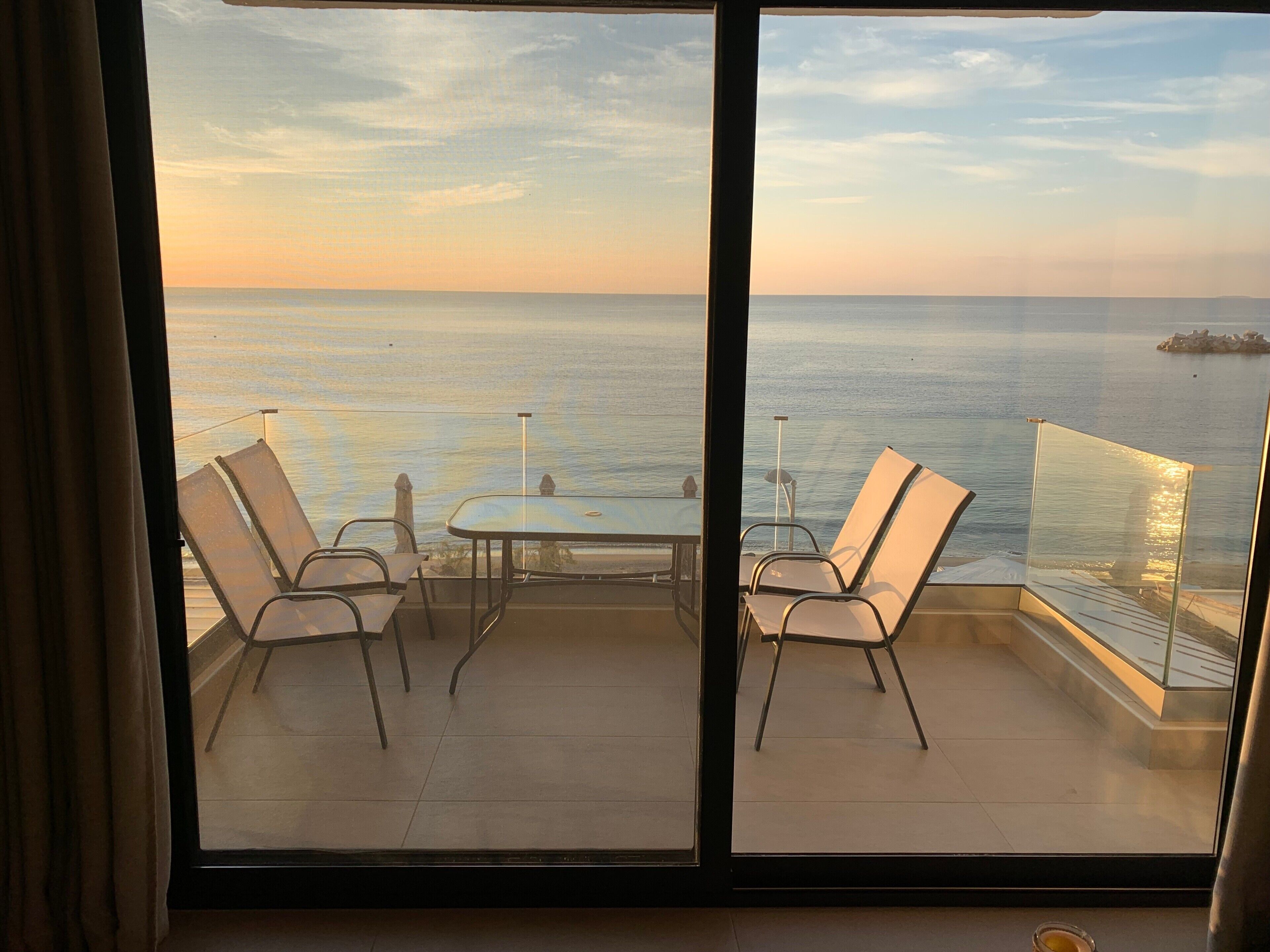 A balcony with two chairs and a table, overlooking a calm sea and a distant island.