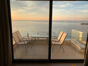 Un balcon avec deux chaises et une table, donnant sur une mer calme et une île lointaine.